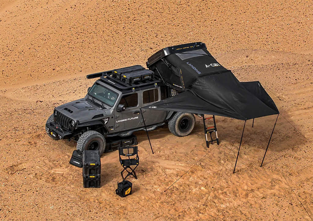 a jeep gladiator with a roof top tent and awning set up with camping chairs.